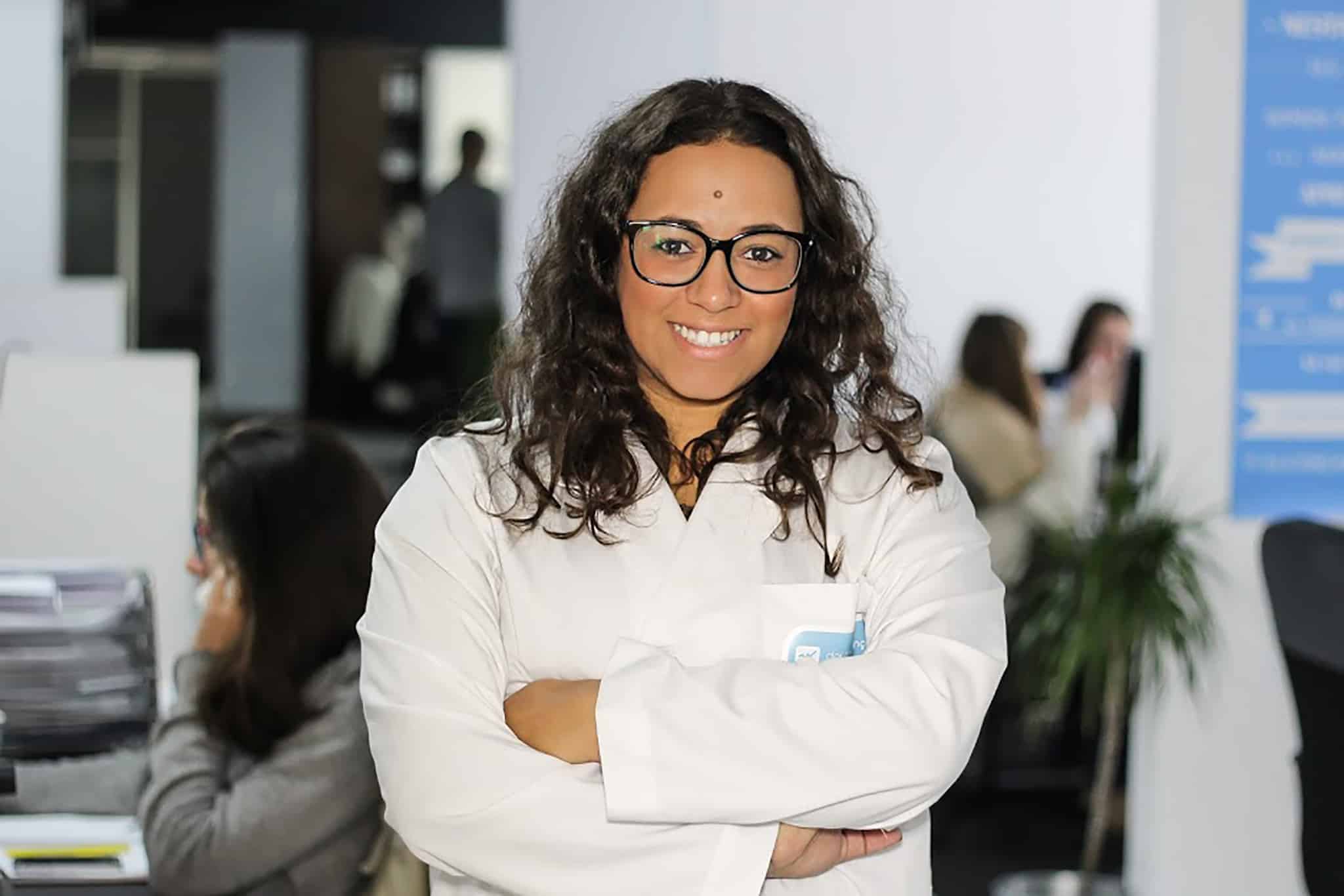 mulher de bata branca, óculos e braços cruzados.