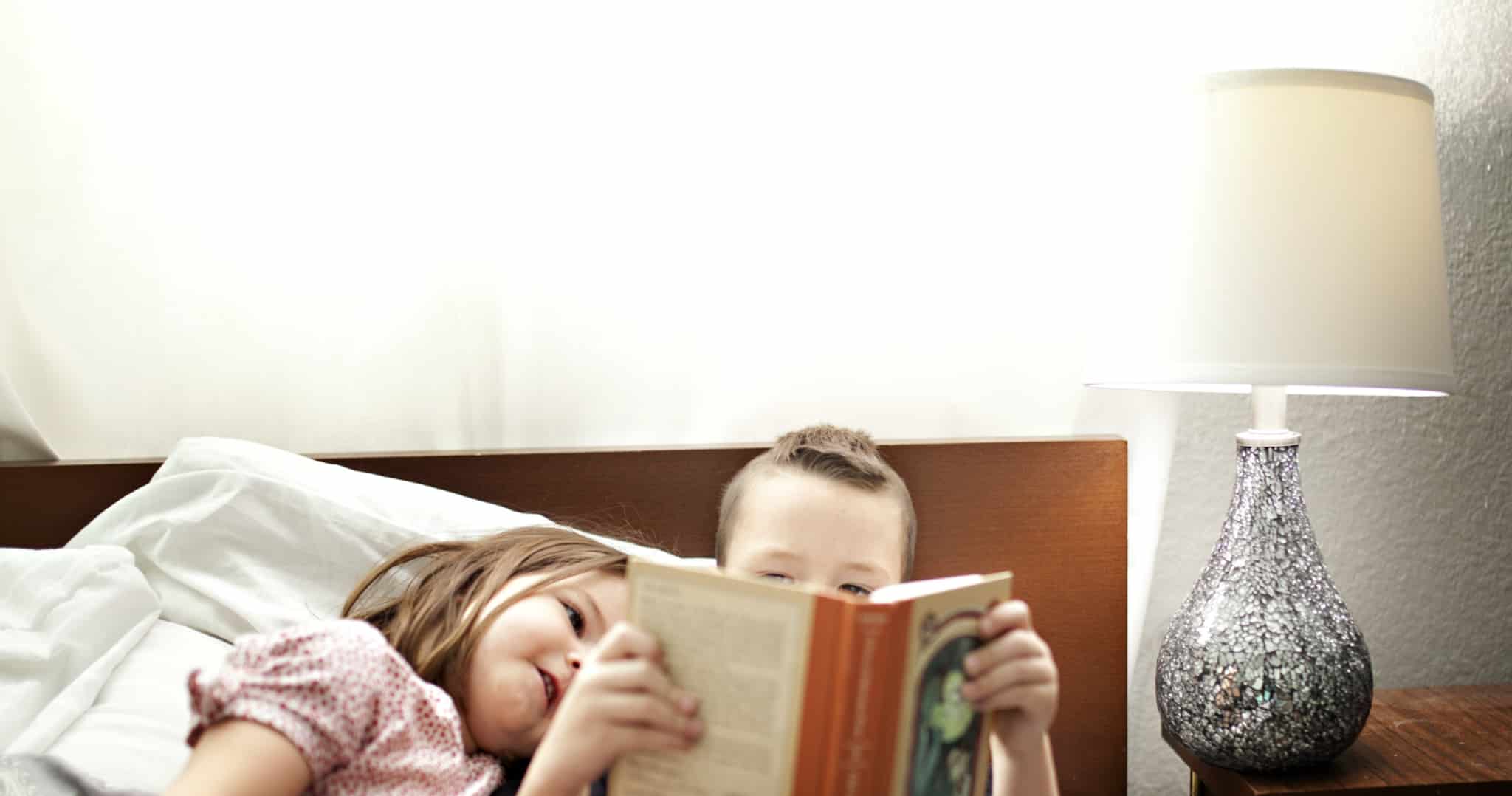 duas crianças a ler um livro ao pé de um candeeiro