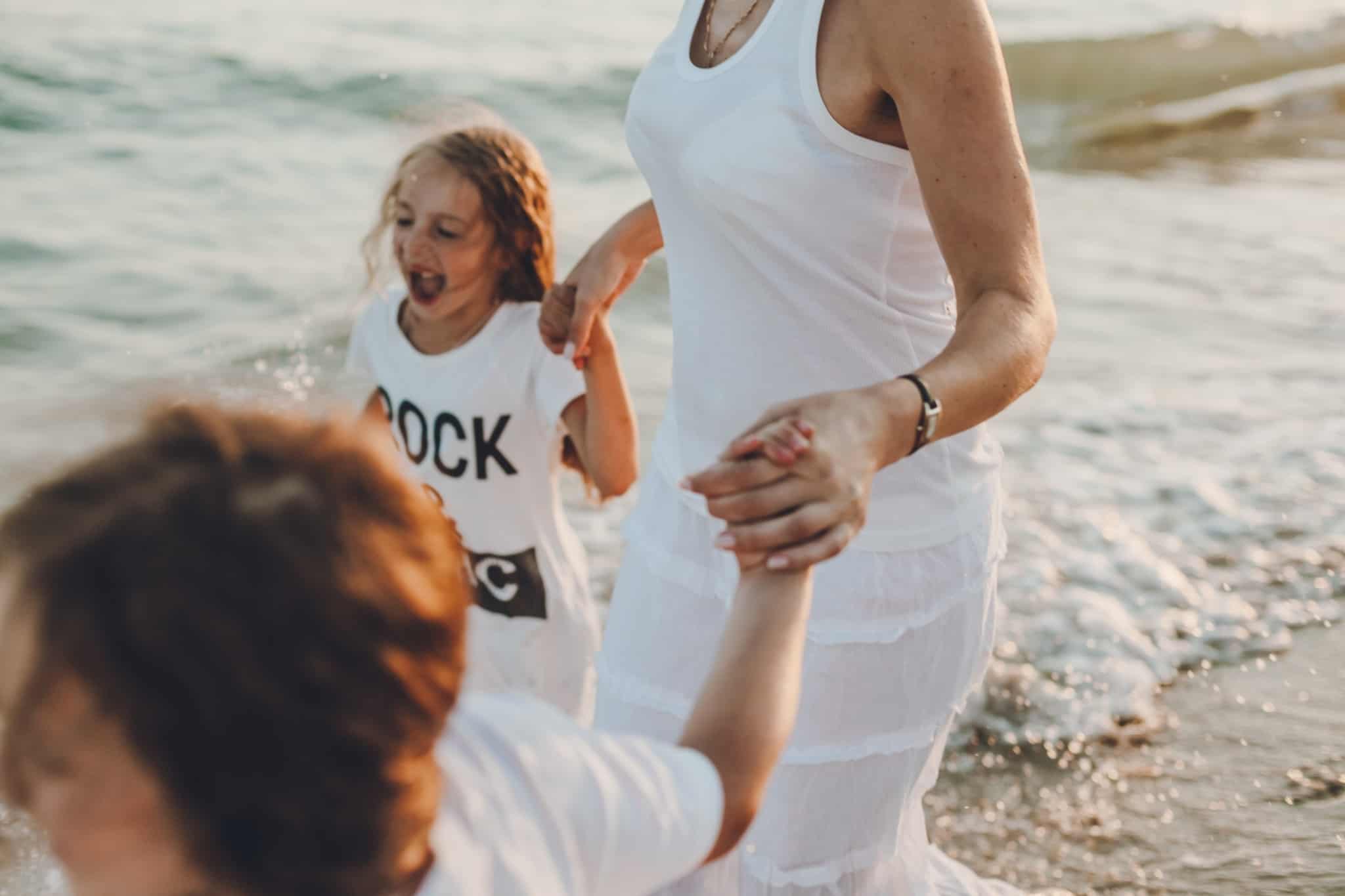 mulher de vestido branco a passear com duas crianças no mar