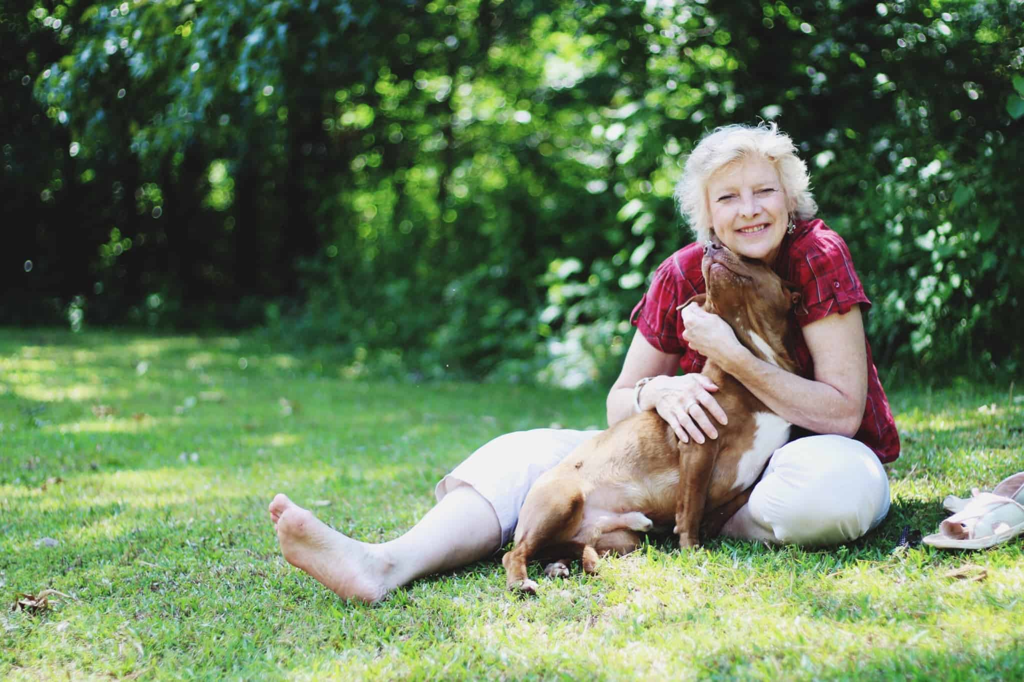 mulher sénior sentada na relva abraçada a um cao castanho