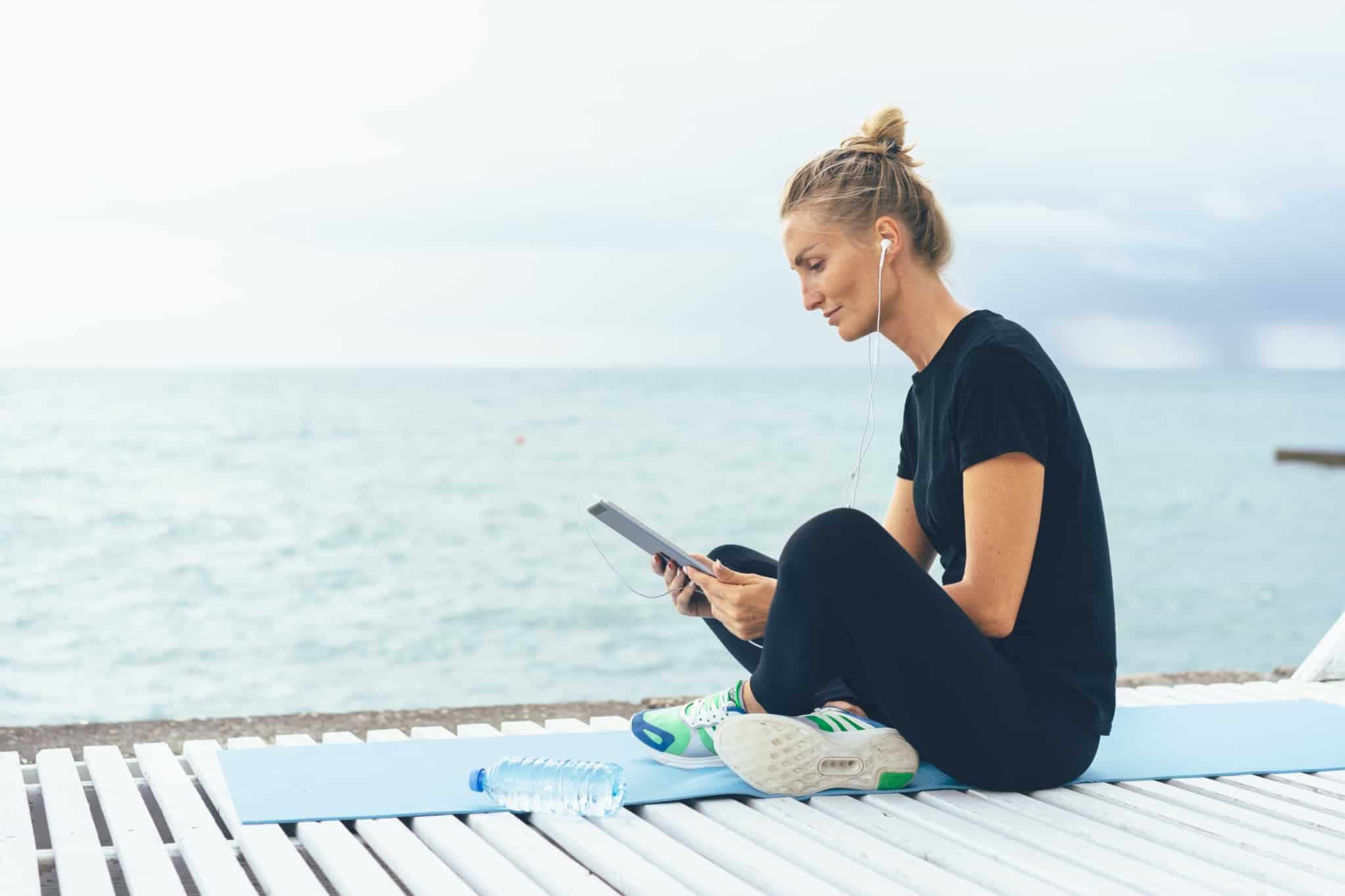 rapariga sentada num tapete de yoga a olhar para o tablet