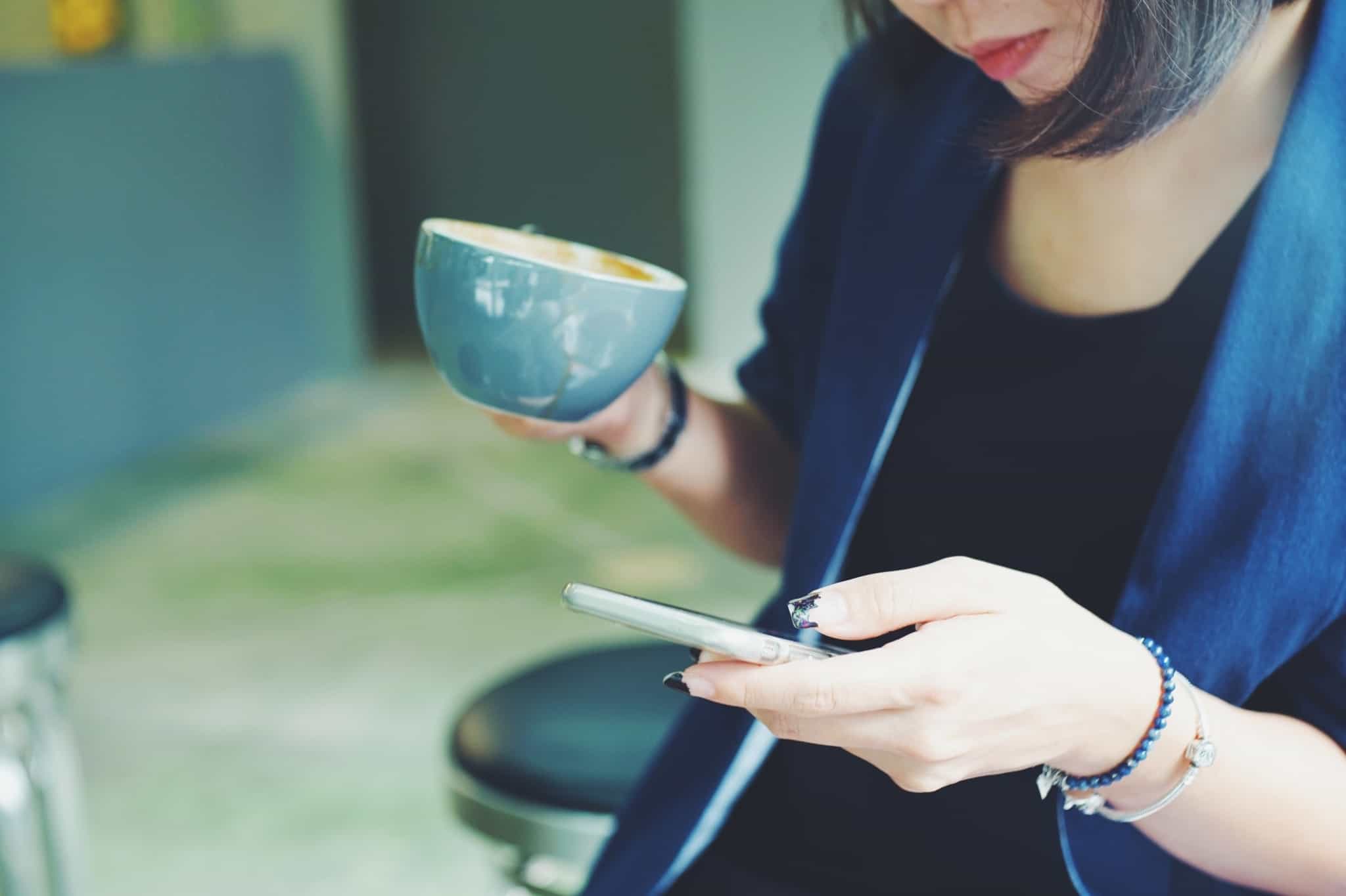 mulher com uma chávena de café e a mexer no telemóvel
